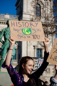 two women holding up signs in front of a building with a statue behind them that says history has given you