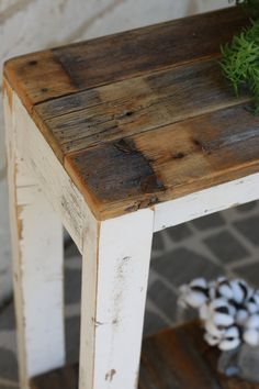 a small wooden table sitting on top of a brick floor next to a pine cone