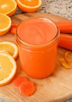 carrots and orange slices on a cutting board next to a jar of juice with an orange slice cut in half