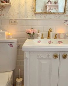 a white bathroom with pink flowers on the sink and mirror above it, along with candles