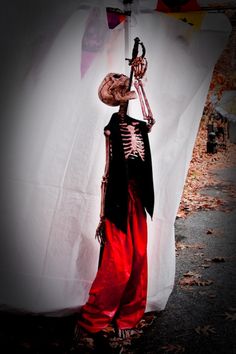 a skeleton dressed in red and black with a hat on it's head standing next to a white sheet