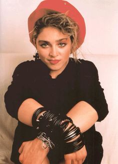 a woman in black shirt and red hat with her arms crossed over her chest wearing bracelets