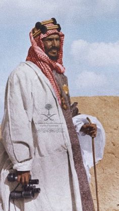 a man standing in the desert with his hat on and holding two canes next to him