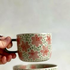 a person is holding a coffee cup in front of two bowls with flowers on them