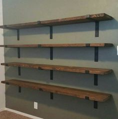 three wooden shelves on the wall in a room with carpeted floor and gray walls