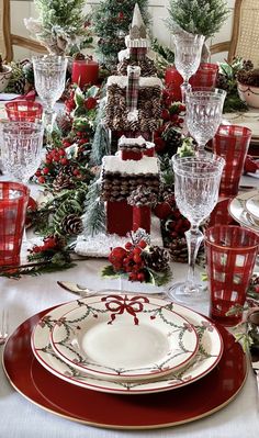 a christmas table setting with red and white plates, silverware and pine cones on top