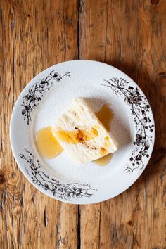 a piece of cheesecake on a plate with butter and syrup in the middle sitting on a wooden table