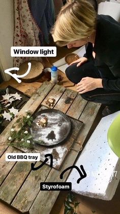 a woman sitting at a table working on an old bbq tray made out of wood