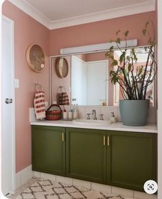 a bathroom with pink walls and green cabinetry, white countertops and a large mirror