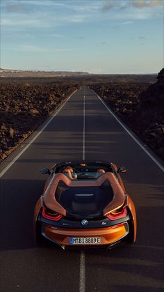 an orange sports car is driving down the road with mountains in the background at sunset