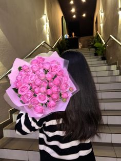 a woman with long hair holding a bouquet of pink roses in front of her face