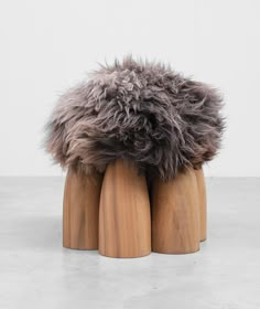 a pair of wooden stools with fur on them sitting on concrete floor next to white wall