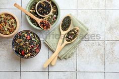 three wooden spoons filled with different types of tea on top of a tiled floor