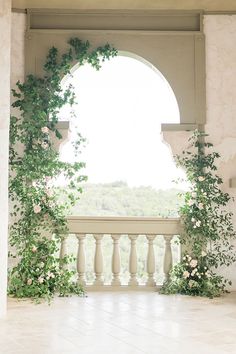 an archway with vines and flowers on the side of a white wall next to a balcony