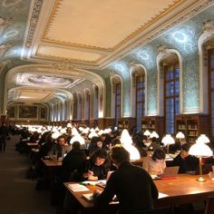 many people are sitting at long tables in the library