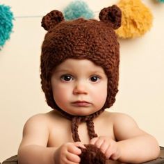 a baby wearing a brown bear hat with pom poms