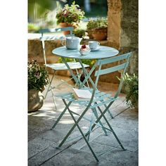 an outdoor table with two chairs and cups on it