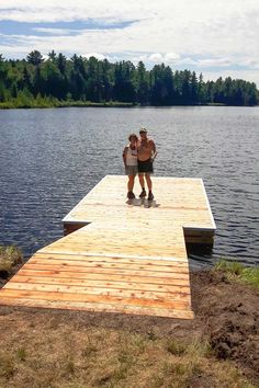 two people are standing on a dock by the water with their arms around each other