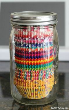 a glass jar filled with colorful cupcakes on top of a table