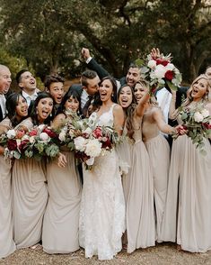 a group of people standing next to each other in front of trees and holding bouquets