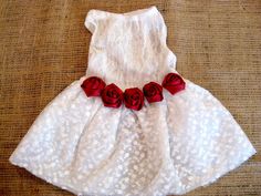 a white dress with red roses on the front and bottom, sitting on a brown surface