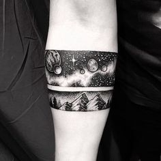 a black and white photo of a man's arm with mountains, stars and planets on it