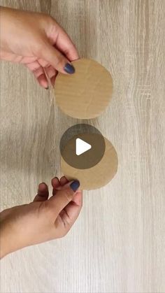 two hands holding cardboard discs on top of a wooden table next to another person's hand