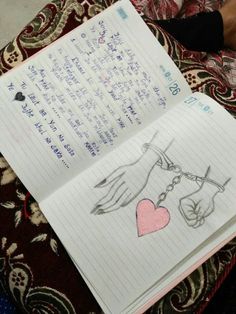 an open notebook with writing on it next to a person's hand holding a heart