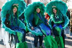 three women dressed in green and blue mermaid costumes, one with her head turned to the side