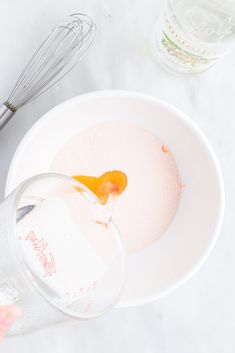 a person pouring liquid into a bowl with a whisk and an orange in it