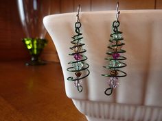 two pairs of earrings are sitting on a white plate next to a glass vase with green and pink beads