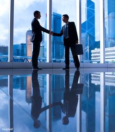 two men shaking hands in front of large windows with cityscape behind them and skyscrapers on the other side