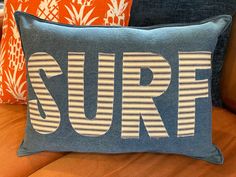 three pillows with the word surf printed on them sitting on a couch in a living room