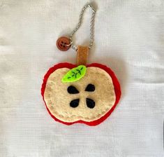 an apple shaped keychain with a green leaf on it's side and a button in the middle