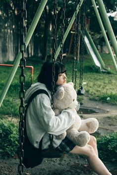 a woman sitting on a swing holding a teddy bear