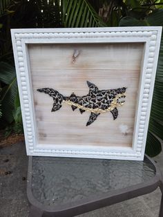 a white frame with a black and gold shark on it's side in front of some plants