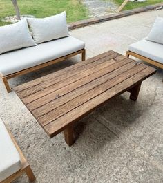 a wooden table sitting on top of a cement floor next to two white couches