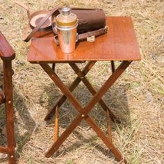 two wooden chairs and a small table with items on it in the middle of a field