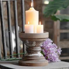 three lit candles sitting on top of a table next to purple flowers and greenery