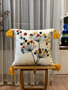 a white pillow with yellow tassels sitting on top of a wooden chair