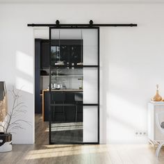 an open door leading to a kitchen and dining room with white walls, wood flooring and black glass doors