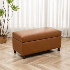 a brown ottoman sitting on top of a wooden floor next to a potted plant