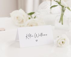 a table with white flowers and a card that says kate williams on the front in black ink