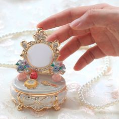 a hand is touching a miniature mirror on top of a jewelry box with pearls around it