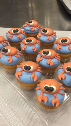 some cupcakes with orange and blue frosting on them are in a plastic container