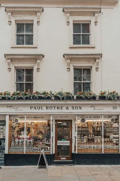 a store front with many windows and plants on the top floor, in front of a white building