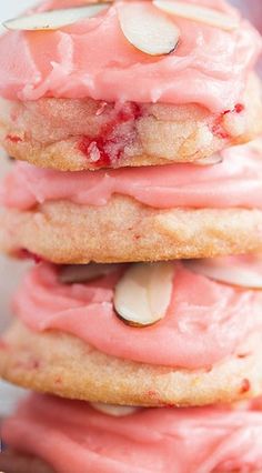 three cookies with pink icing and almonds on top are stacked up in front of each other