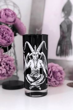 a black glass with an image of a demon on it and flowers in the background