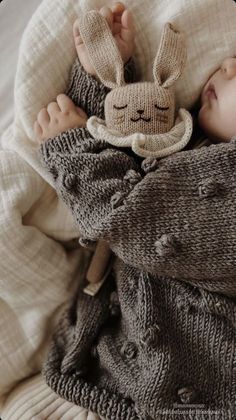 a baby sleeping in a bed with a knitted bunny hat and sweater on it's head