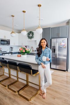 a woman standing in front of a kitchen island with stools and a coffee cup